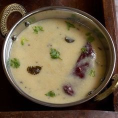 a metal bowl filled with soup on top of a wooden table next to a spoon