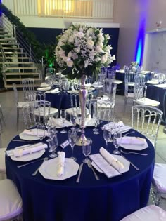 a table set up for an event with blue linens and white flowers in the center