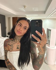 a woman with tattoos taking a selfie in the mirror while holding up her phone