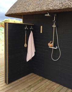 a bathroom with black walls and wooden flooring next to a bathtub, shower head, and towel hanging on the wall