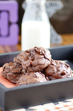 chocolate cookies are stacked on top of each other in a black tray next to a glass of milk