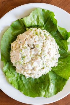 a white plate topped with lettuce and chicken salad on top of a wooden table