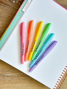 four pens sitting on top of a notepad next to an open notebook with writing