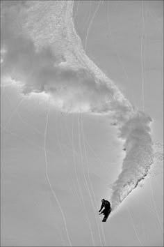 a snowboarder is going down a snowy hill in front of a large wave