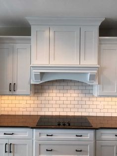 a kitchen with white cabinets, black counter tops and an oven hood over the stove