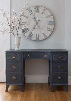 a clock mounted to the side of a wall next to a blue desk with drawers