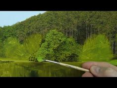 a person is holding a paintbrush in front of a painting of trees and water