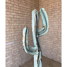 a large blue metal cactus sculpture in front of a brick wall on concrete flooring