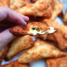 a hand holding a piece of food with cheese and sauce on it, in front of some fried crackers