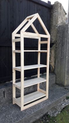 a wooden shelf sitting on the side of a road next to a black building and grass