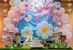 a table topped with lots of balloons and cake next to a wall covered in flowers