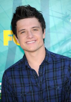 a smiling young man with black hair and blue shirt in front of a green background