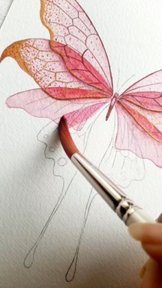 someone is drawing a butterfly with watercolors on paper and using a brush to draw the wings