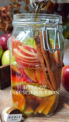 apple pie infused bourbon being poured into a mason jar with cinnamon stick and apples in the background