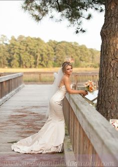 a woman in a wedding dress standing on a bridge next to a tree and looking at the camera