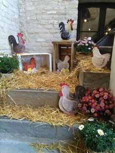 chickens and roosters are sitting on hay in front of a building with flowers growing out of it