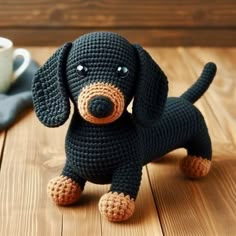 a crocheted black dog sitting on top of a wooden table next to a cup