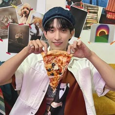 a boy holding up a slice of pizza in front of his face with pictures on the wall behind him