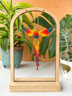 a colorful beaded bird hanging from a wooden frame on a table next to potted plants