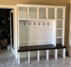 an empty room with white shelves and hooks on the wall, along with tile flooring