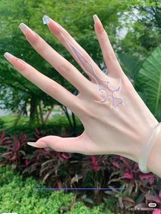 a woman's hand with white and blue nail designs on it, in front of some plants