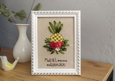 a pineapple with flowers is framed in a white frame next to a small vase