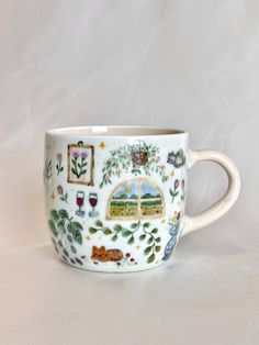 a coffee cup decorated with animals and plants on it's side, sitting on a white surface