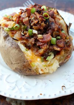 a baked potato topped with bacon and green onions on a white plate next to a fork