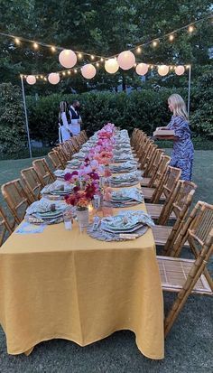 a long table is set up with plates and silverware for an outdoor dinner party