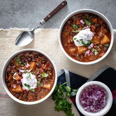 two bowls of chili with sour cream on top and red onion garnish in the bottom