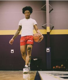 a young man holding a basketball on top of a hard wood floor in a gym