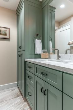 a bathroom with green cabinetry and white counter tops, along with a large sink