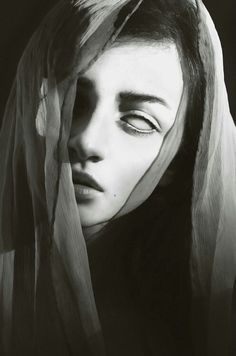 a black and white photo of a woman's face with veil over her head