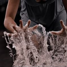 a young boy is playing in the water with his hands out to catch something while wearing a black shirt