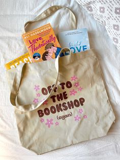 a tote bag with books on it sitting on a bed next to a pillow