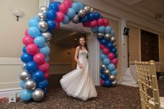 a woman in a wedding dress standing under a balloon arch at the entrance to a banquet hall