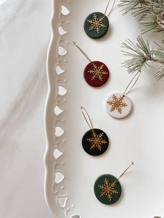 four ornaments are sitting on a white platter next to pine branches and snowflakes