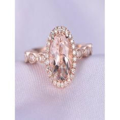 an oval shaped morganite and diamond ring on top of a white cloth with diamonds around it