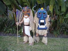 two people dressed in costumes standing next to each other on the grass with palm trees behind them