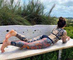 a woman sitting on top of a wooden bench covered in lots of tattooed tattoos and leggings