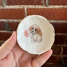 a hand holding a small white plate with a brown and white dog on it's side