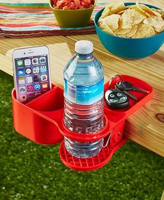 a water bottle and cell phone holder on a picnic table with chips, remotes and drinks