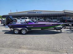 a purple and green boat is parked in front of a building with other vehicles behind it