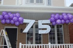 purple balloons are hung over the front door of a house for an 75th birthday party