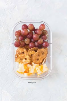 grapes, cheese and crackers in a plastic container on a white surface with water