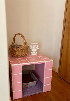 a pink and white dog house with a basket on top of it's shelf