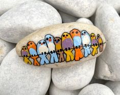 a painted rock with birds on it sitting in front of some white rocks and pebbles