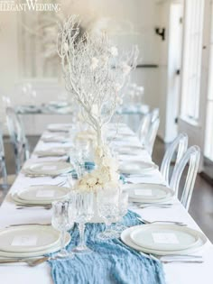 a table set with white and blue place settings, silverware and flowers in vases