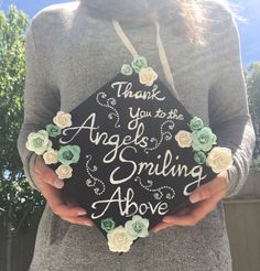 a woman holding a graduation cap with flowers on it that says thank you to the angels smiling above