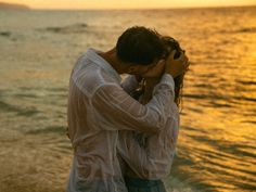 a man and woman are kissing on the beach at sunset, with water in the background